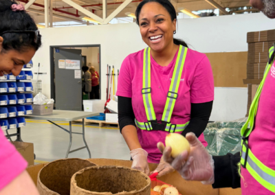 Smiling volunteer in a neon safety vest and pink shirt bagging onions in a warehouse food distribution setting.