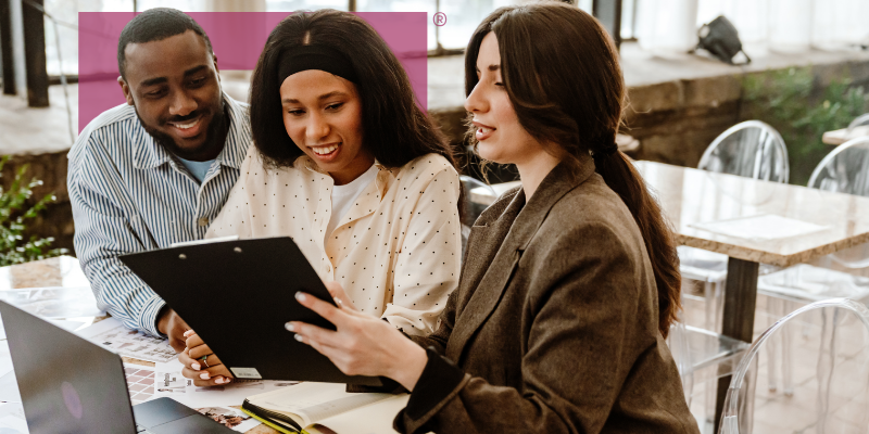 alternative lending as a strategic tool | Magenta Capital Corporation Three colleagues review a clipboard together at a cafe table, smiling while collaborating—informal business meeting outside.